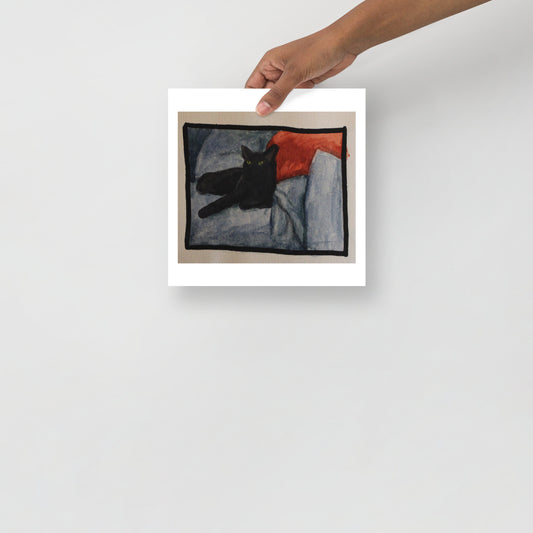 Product mockup of a watercolor painting that depicts a black cat lying on a textured blanket with a red pillow