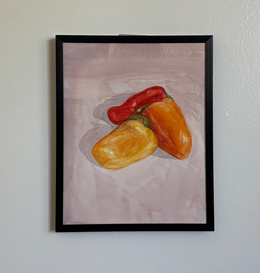 A framed still life painting of three bell peppers (one red, one orange, and one yellow) on a textured light pink background, housed in a black frame and hung on a white wall.