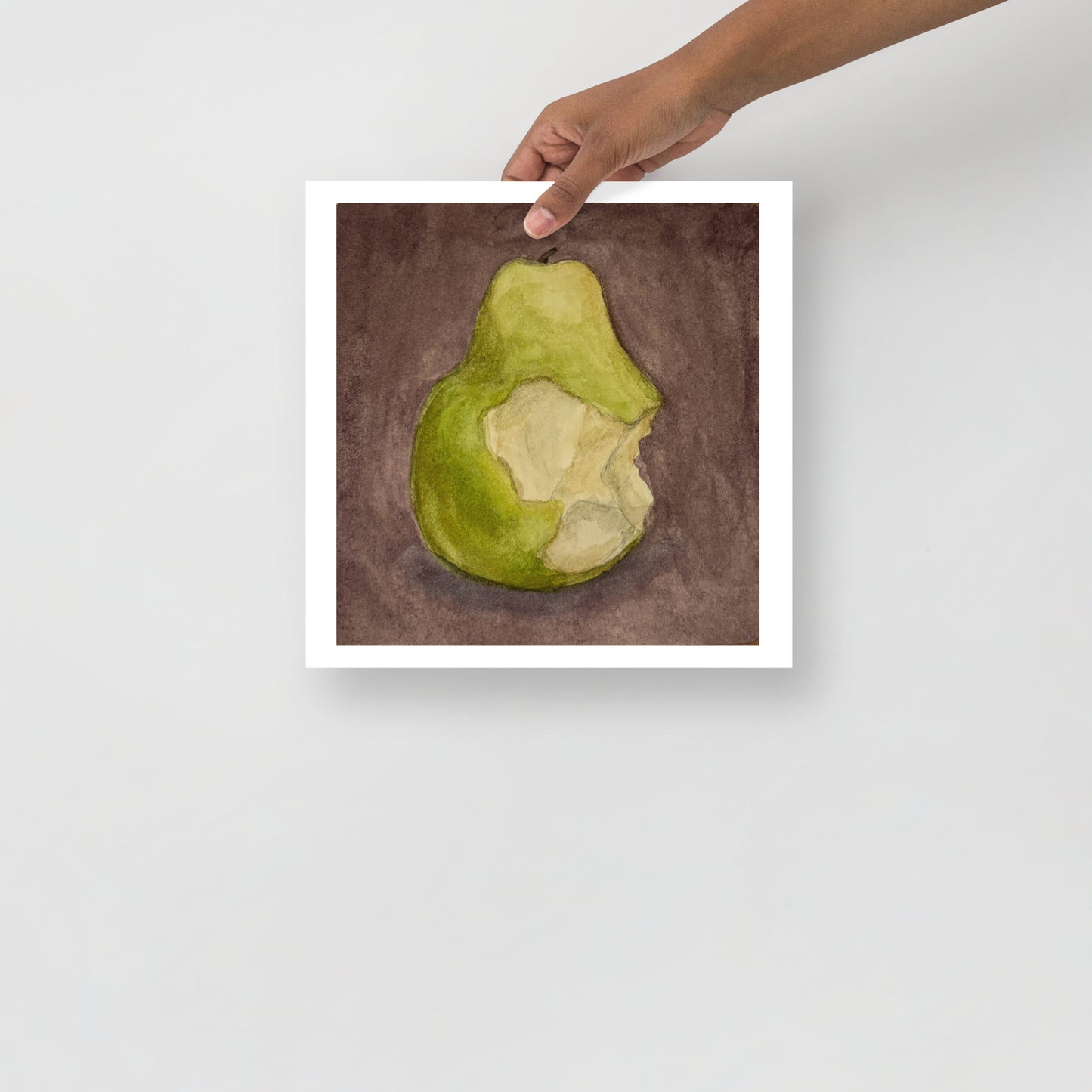 Product mockup image includes a hand holding a print of my painting of a green pear with a bite taken out of it against a plum colored background. 