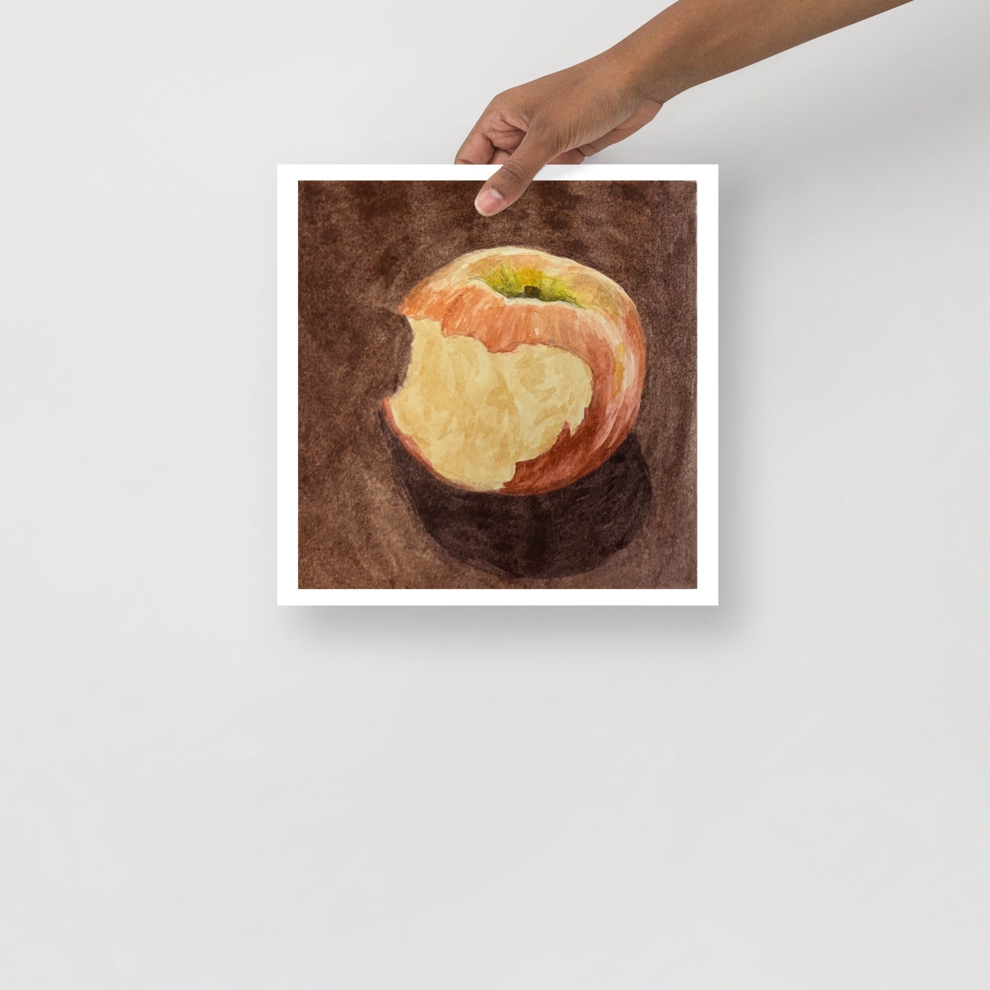 Product mockup of a watercolor painting print that depicts a red apple with a bite against a brown background 