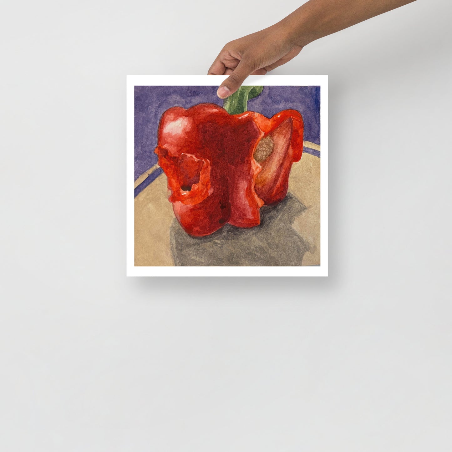 Product mockup of a watercolor painting of a red bell pepper with bites taken out of it on a textured surface with a dark background