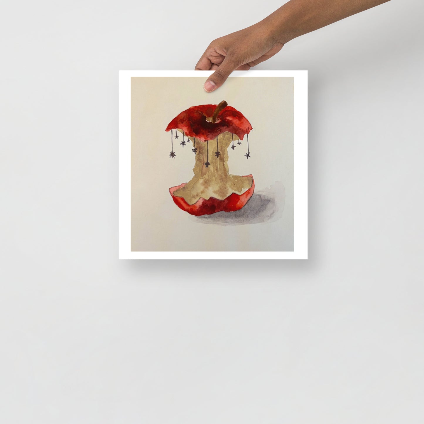 Product mockup of a watercolor painting print of a red apple with a bite taken out, hanging stars, and a beige background.