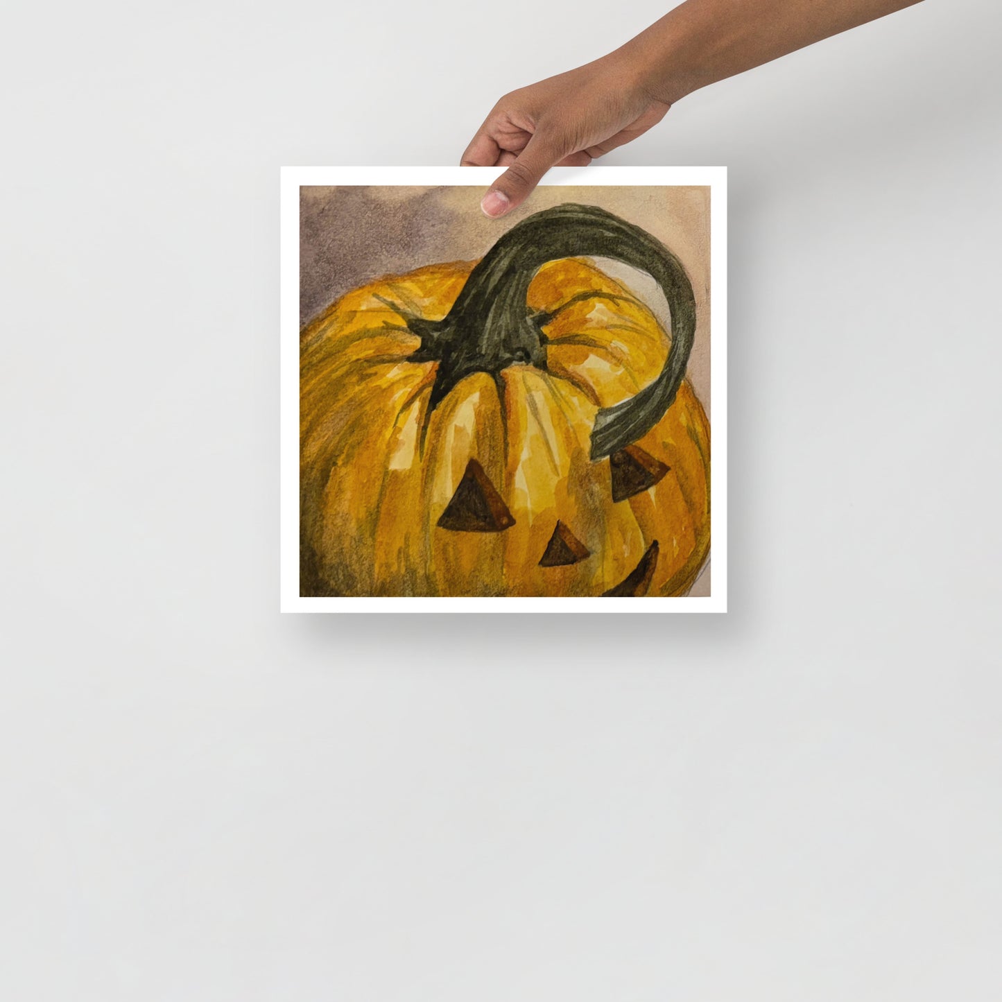 Product mockup of a watercolor painting print that depicts a pumpkin with a face carved into it on a textured beige background.