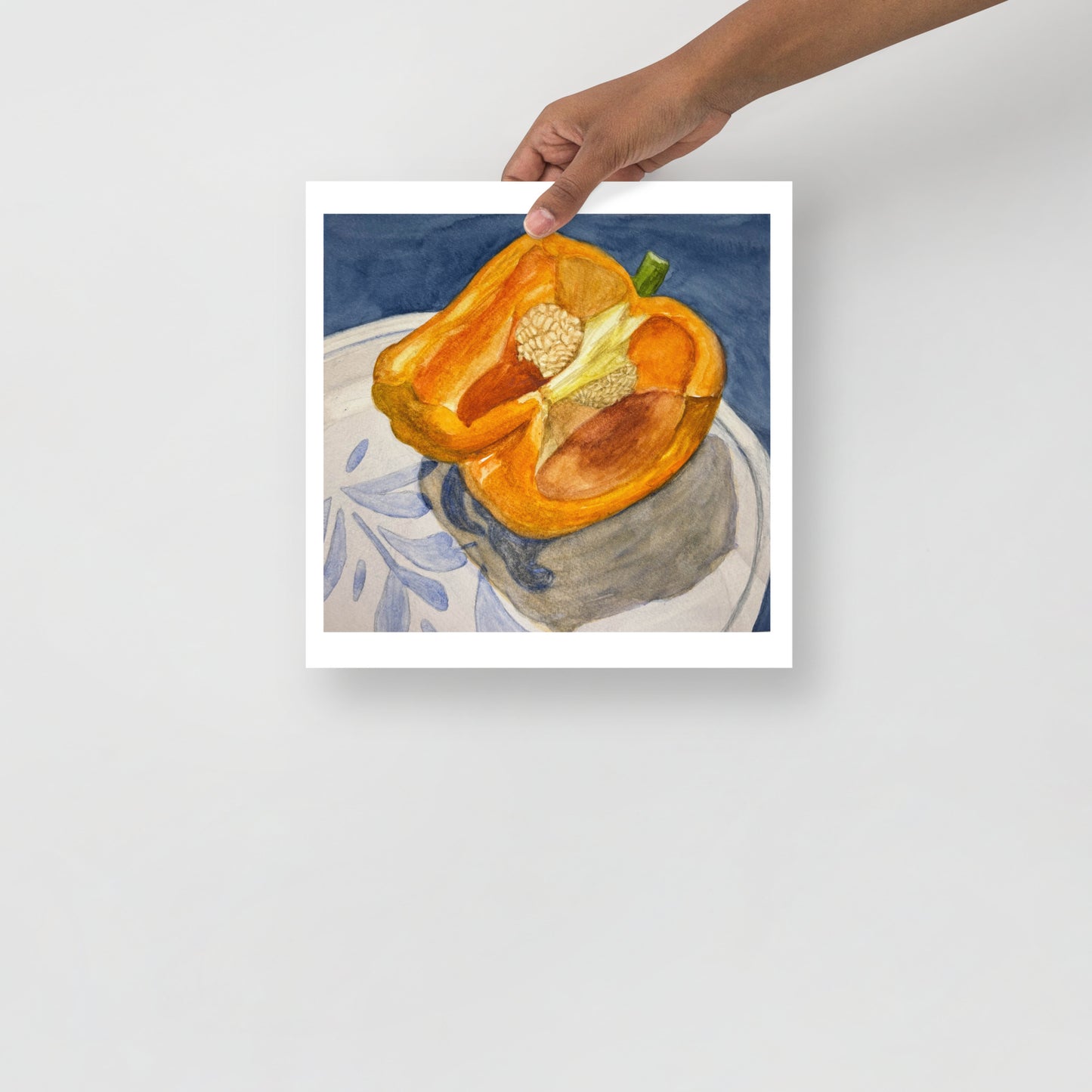 Product mockup of watercolor painting of a halved orange bell pepper on a white plate with a design against a blue background. 
