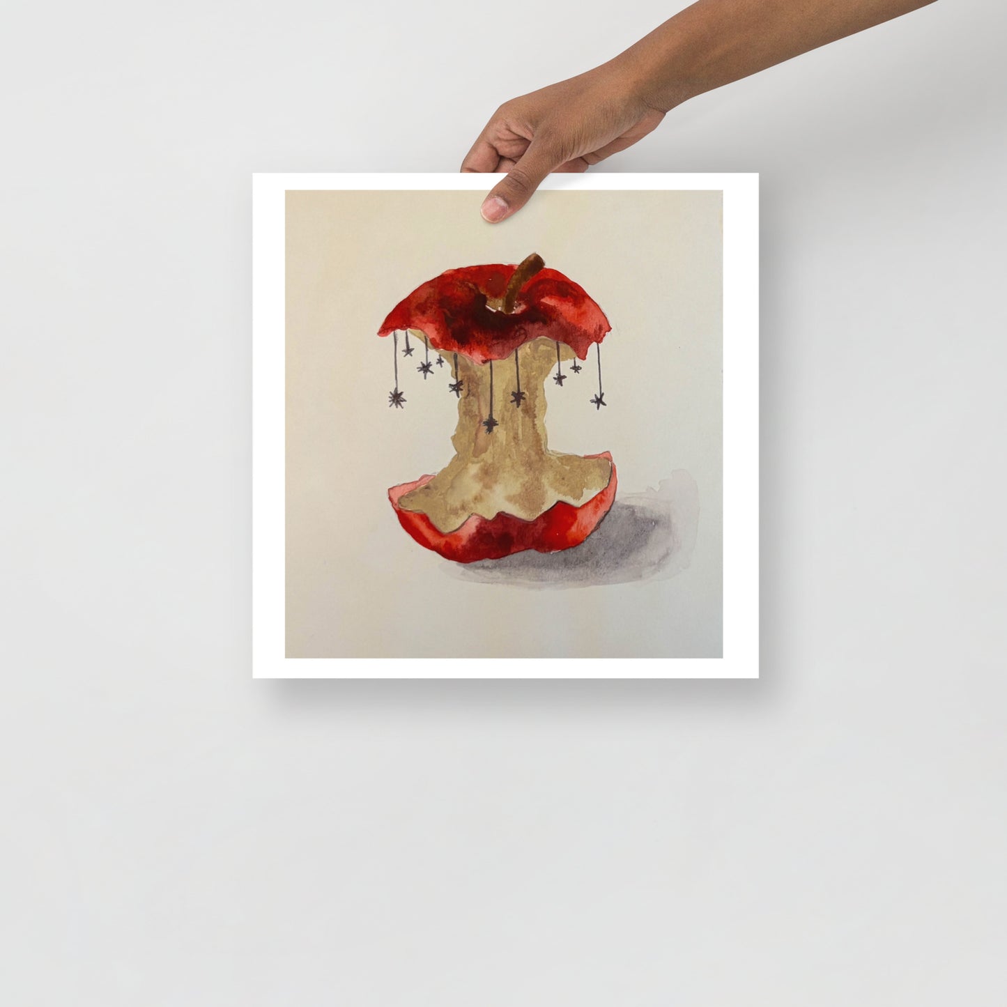 Product mockup of a watercolor painting print of a red apple with a bite taken out, hanging stars, and a beige background.