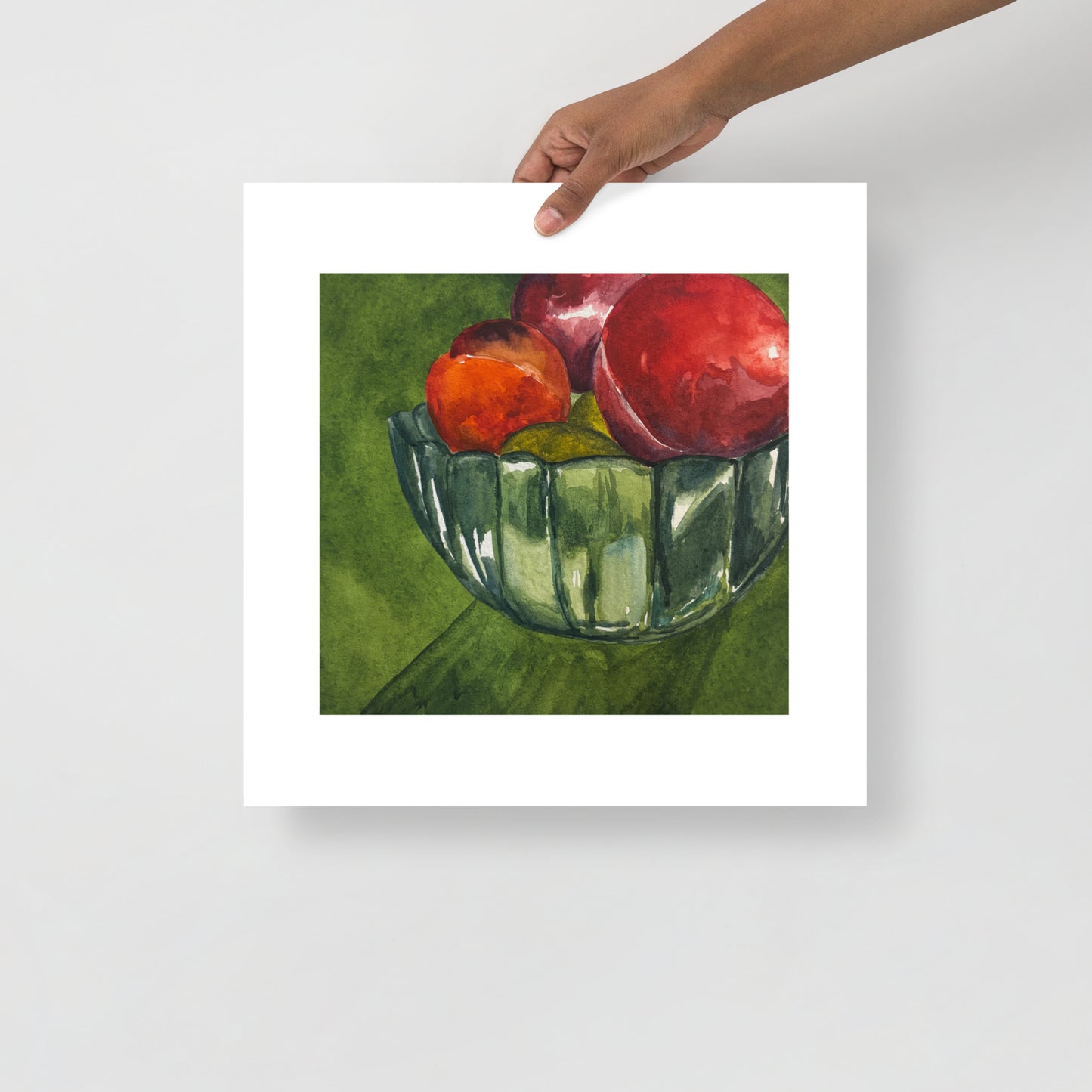 Product mockup of a watercolor painting print that depicts a green bowl with red fruit against a green background. 
