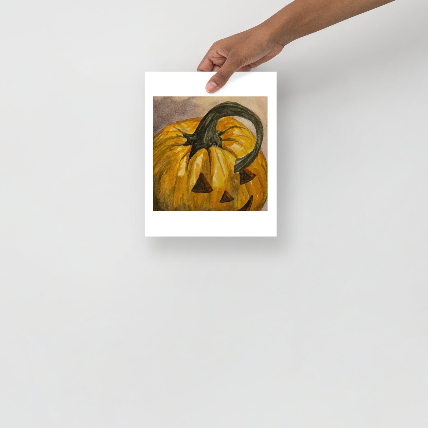 Product mockup of a watercolor painting print that depicts a pumpkin with a face carved into it on a textured beige background.
